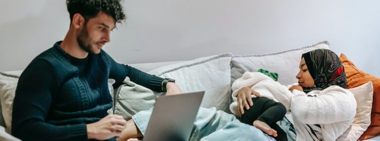 couple with baby on couch looking at laptop